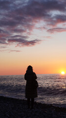 Fototapeta premium Silhouette of woman standing by the ocean during sunset with colorful sky