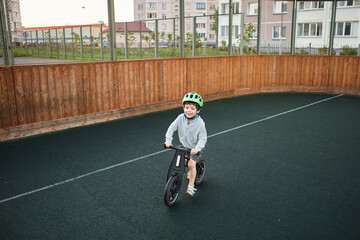 Young boy riding balance bike with green helmet on sports court