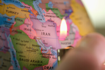 A person holds a lighter near a colorful map of Iran, illuminating the outline of the country and...