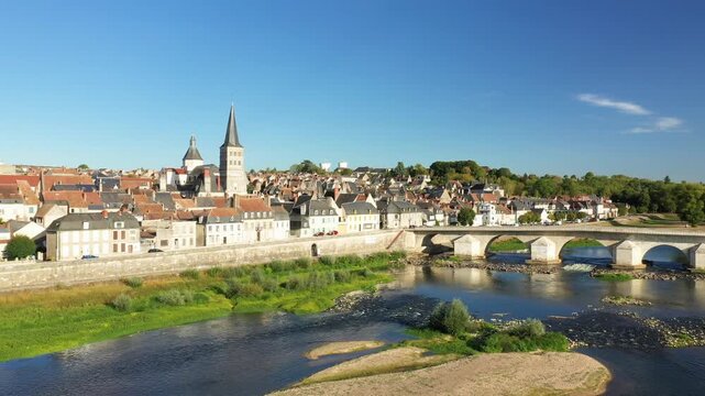 Scenic aerial view of La Charite sur Loire with its iconic stone bridge and church towers along the Loire River under a clear blue sky. Picturesque French village landscape with traditional