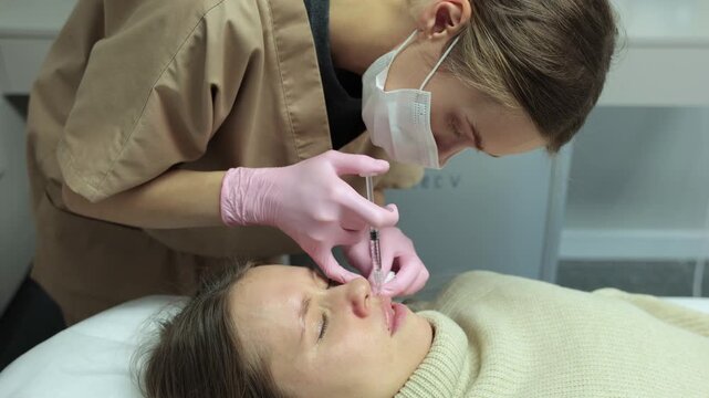 Professional cosmetologist in mask and pink gloves performing Botox injection to female client's upper lip area in a clinic. Medical beauty treatment for wrinkle correction