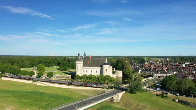 Drone shot of the historic Chateau de Sully sur Loire with surrounding village and lush greenery under a clear blue sky in France.