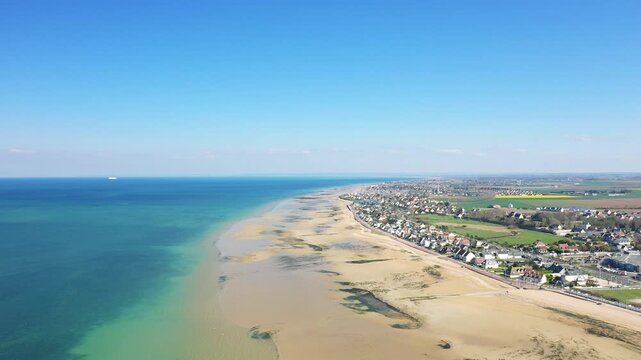 A stunning aerial view of Juno Beach and the coastal town of Bernieres sur Mer, with clear blue skies and turquoise waters along the Normandy coastline.