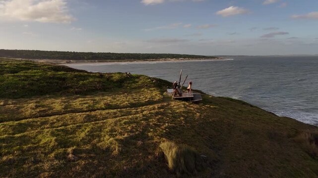 A couple stands at Cerro Chato viewpoint looking out over the Atlantic Ocean during sunset.