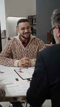 Vertical view of cheerful young candidate talking with two HR managers during job interview at white desk with applications forms on it