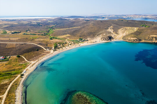 High-angle aerial view of the Neftina Beach on Limnos Island, Greece, showing crystal clear turquoise waters meeting a sandy shoreline backed by rugged, arid Mediterranean hills.