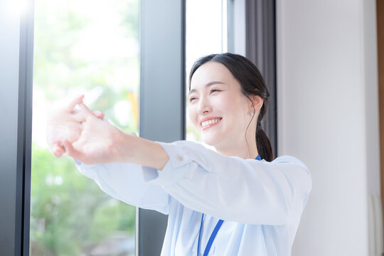 新緑の会社の窓際で伸びやストレッチする休憩するビジネスシーンの女性　スッキリして気分爽快