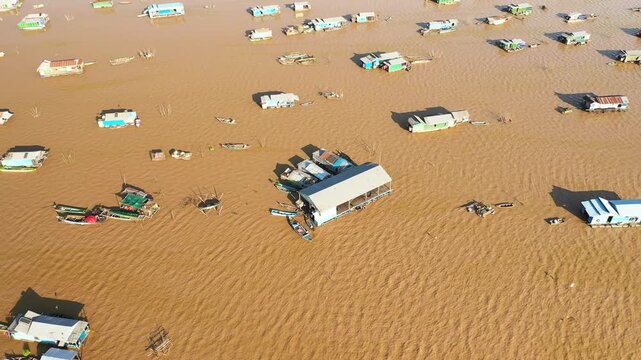 Aerial view of floating houses and boats scattered across muddy water in the Chong Kneas floating village, Cambodia. Unique rural lifestyle and water based community captured from above.