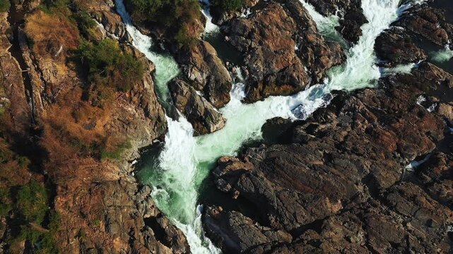 Dramatic aerial shot of Tat Somphamit Waterfalls, also known as Li Phi Falls, with rushing water cutting through rugged rocks at sunrise in Laos.
