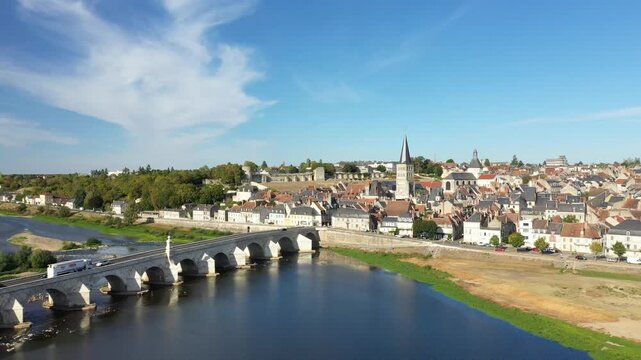 Scenic aerial shot of La Charite sur Loire, France, featuring a historic stone bridge over the Loire River and charming old town architecture under a clear blue sky.