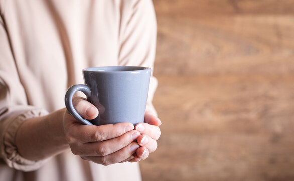 Gray ceramic mug balanced on a hand in front of a brown wall, beverage, minimalist style, studio shot.