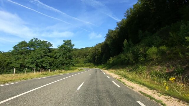 Empty winding road passing through lush green forest in the Morvan region of France on a sunny summer day. Scenic rural landscape ideal for travel and nature concepts.
