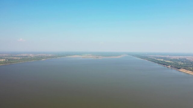 Wide aerial shot of the West Baray reservoir with calm water and surrounding landscape under a clear blue sky in Cambodia.