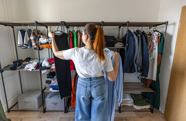 Obraz premium Young woman is choosing clothes from her closet