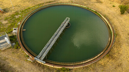 Aerial view of a circular wastewater treatment tank filled with green water. Closeup of a metal...