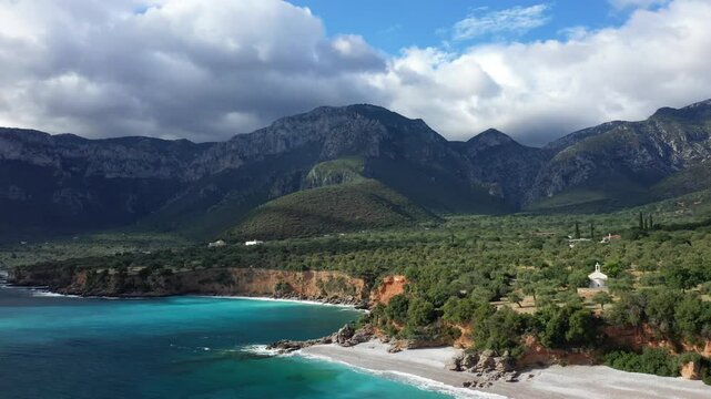 Scenic coastline with turquoise waters, rocky cliffs, and lush green hills near Monemvasia, Greece, under a dramatic cloudy sky.