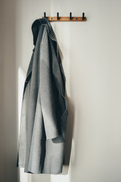 A cozy classic grey coat on a hanger, hanging on a wall with minimalist daylight.