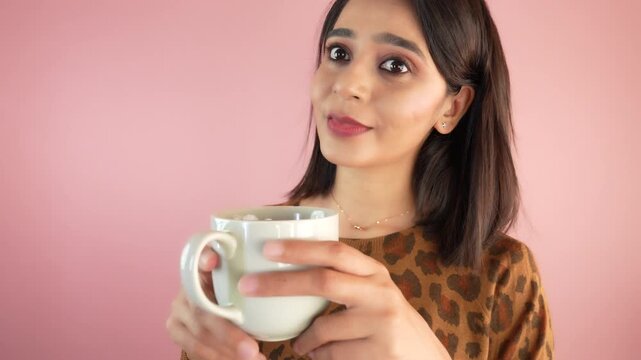 Close up of happy thoughtful pretty young Asian woman girl hold coffee cup thinks ideas feels happiness look at camera, isolated over light pink studio background.