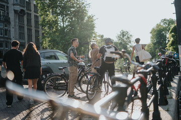 A group of friends stand with bicycles on a sunlit Dutch street. The friends chat and prepare to cycle through the city in warm afternoon light.