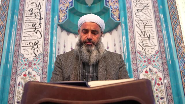 A Muslim sheikh reading the Qur&rsquo;an in the mihrab of the mosque, an elderly Muslim man praying during Ramadan. Concept of religions, Eid al-Fitr.