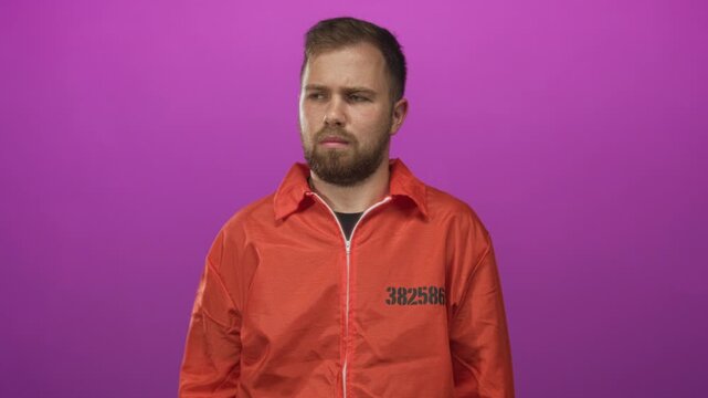 Man in orange prison jumpsuit frowning in purple studio with inmate number visible on chest, head and shoulders framed; unease.