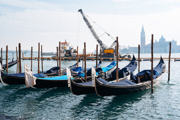 Fototapeta premium Gondolas moored at waterfront with cranes and buildings in the background during daytime in Venice