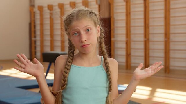 Portrait thinking Caucasian little daughter girl kid think unsure shrug shoulders shrugging doubtful child gymnast acrobat feeling doubt pondering idea in school gym pupil teenager in sport class