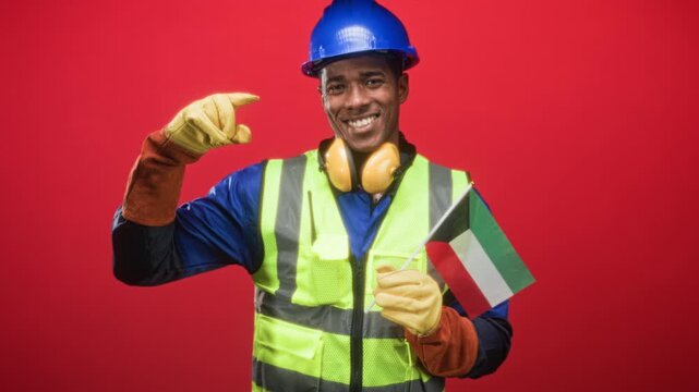 Man construction worker in hardhat holding kuwait flag points finger to flag in studio; pride solidarity support.