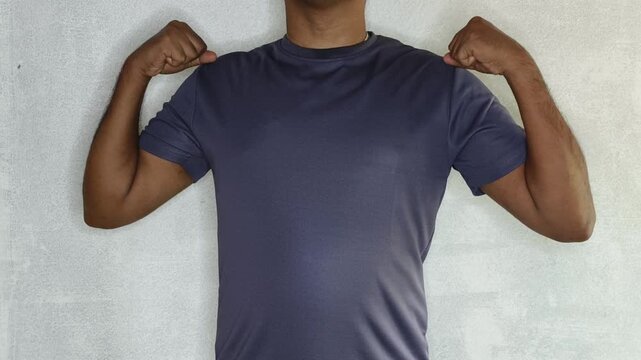Strong indian or asian man flexing biceps and arm muscles wearing workout t-shirt. Muscular male doing upper body strength pose after gym training to check muscle growth. Healthy lifestyle concept.