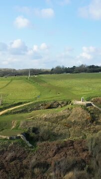 Wide view of grassy hills and historic concrete bunkers at Omaha Beach WN 62 in Normandy, France, under a partly cloudy sky.