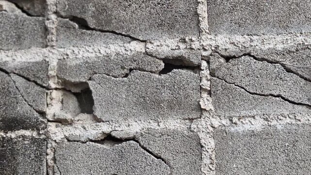 An old white brick wall, worn and cracked, possibly from foundation issues, weathered materials, or the force of an earthquake.