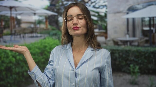 Woman wearing eyeglasses and striped shirt palm up gesture at restaurant building terrace; contemplation.