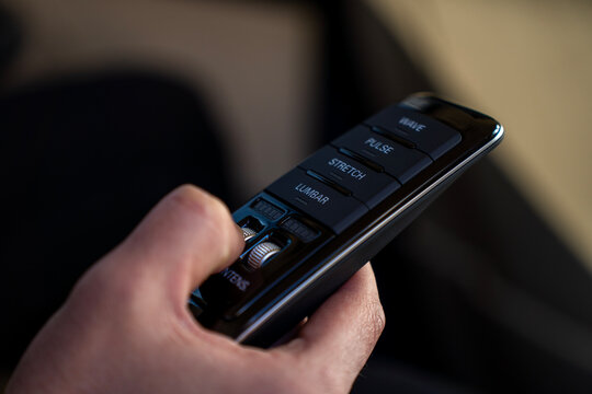 Passenger controlling seat massage function using remote control with massage modes and intensity adjustment in luxury car interior.