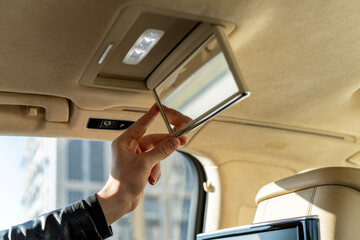 Naklejka premium Hand opening illuminated vanity mirror integrated into car ceiling panel inside luxury sedan interior.