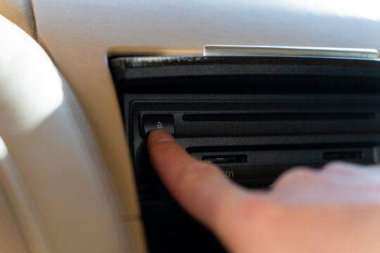 Passenger pressing eject button of car multimedia CD player in the center console of a luxury vehicle.