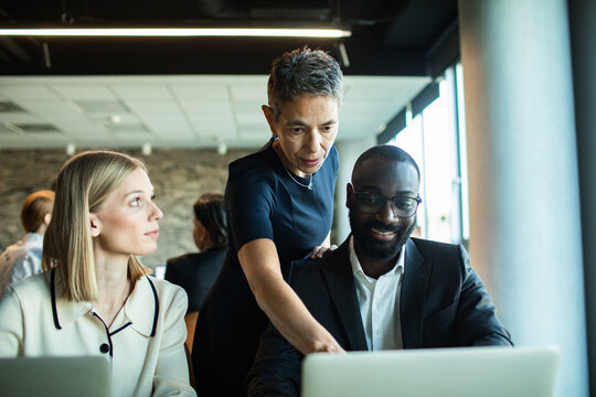 Manager mentoring coworkers on laptop in modern office