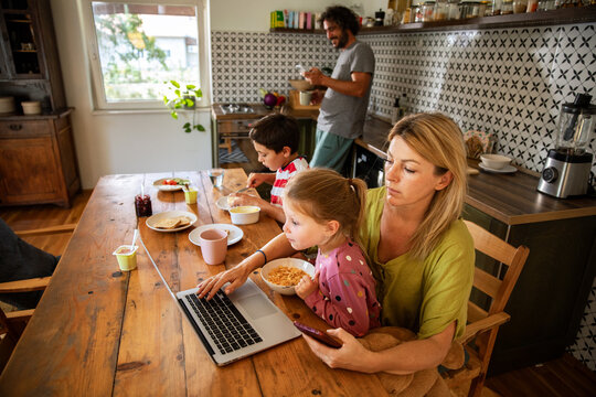 Parents working remotely while kids eat breakfast in home kitchen
