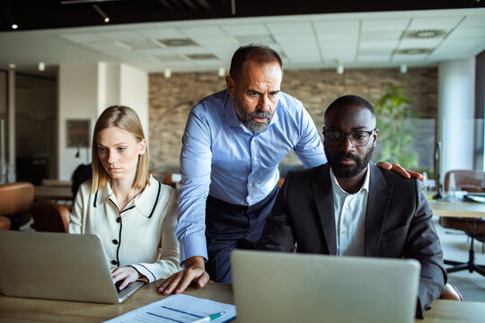 Senior manager coaching coworkers on laptops in modern office