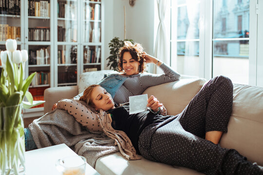 Two women relaxing on sofa at home with pregnancy ultrasound photo