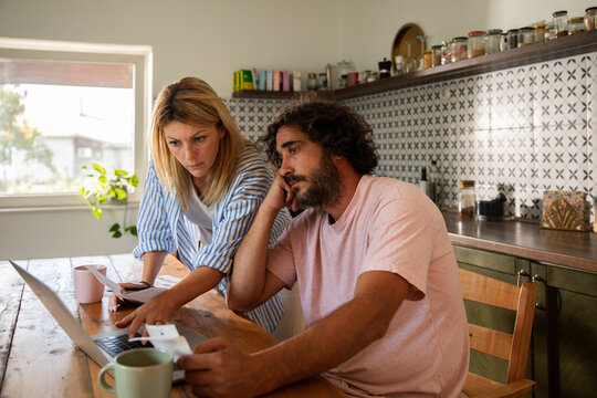 Concerned couple reviewing bills on laptop at kitchen table