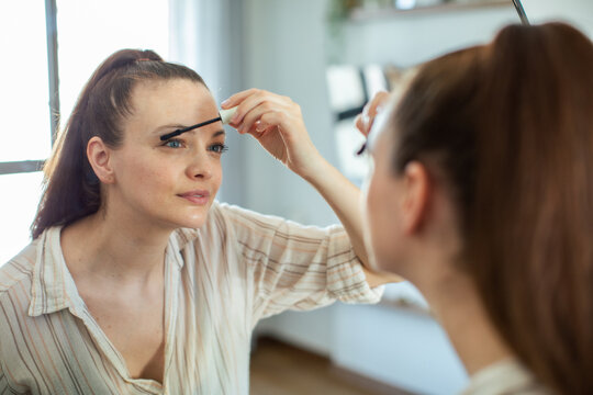 Young woman applying mascara in bathroom mirror
