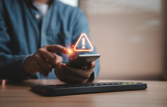 Person using smartphone with warning alert notification symbol on screen for cybersecurity risk, online fraud detection, mobile security protection and digital threat awareness concept.