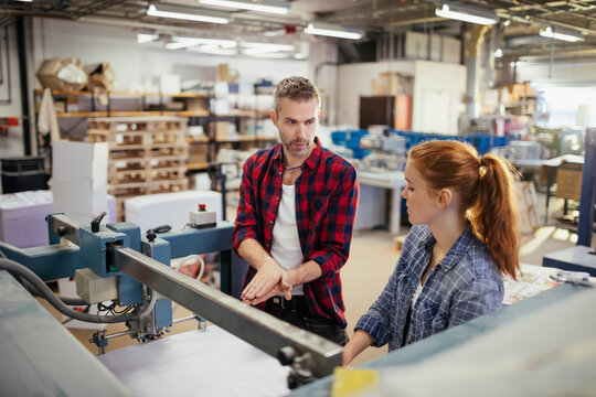 Supervisor training employee on industrial printing machine in factory