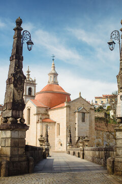 Stone bridge leading to the domed church of Sao Goncalo in Amarante, Portugal, framed by historic lanterns under a blue sky.