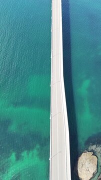 Vertical aerial drone view of cars driving across a straight bridge over emerald green sea in Japan - 13