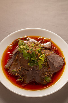 Braised beef slices in chili oil and sesame, cilantro garnish on glossy red pool, rich tender meat offering bold savory heat. Close-up plate with traditional Chines food. 