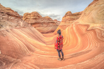A woman stands in a canyon with a red blanket draped over her shoulders © ExploringandLiving