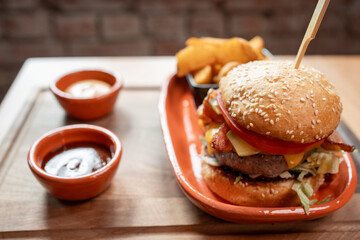 Juicy burger served with crispy fries and tangy dipping sauces on wooden table