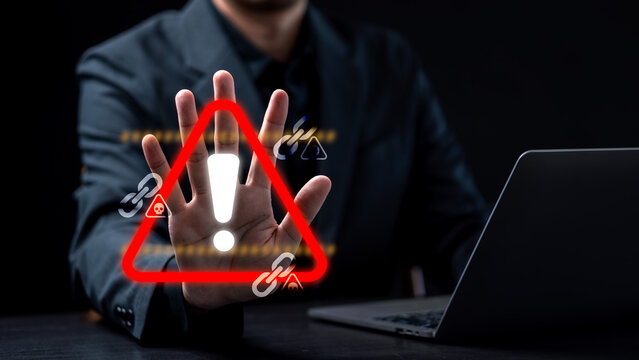 Cybersecurity threat prevention and digital risk warning concept. Businessman showing a stop hand gesture to a glowing red alert triangle, broken links, and malware skull holograms.