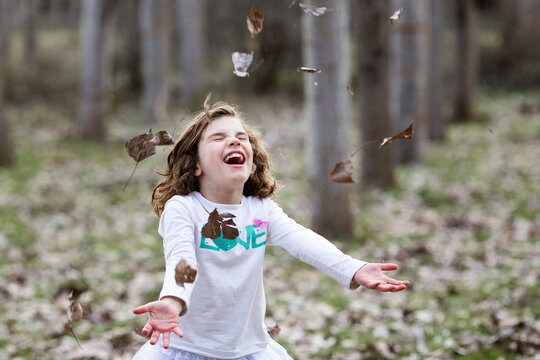 Happy Girl standing in an autumnal forest throwing autumn leaves in the air, Granada, Andalucia, Spain